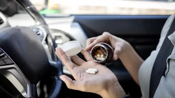 Frau nimmt Ibuprofen im Auto ein. Vorsicht beim Autofahren nach Medikamenteneinnahme.
