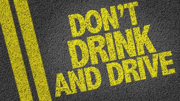 Gelbe Schrift auf Asphalt: "DON'T DRINK AND DRIVE". Informiert über die Promillegrenze Italien.