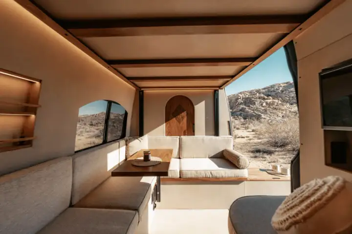 Gemütlicher wohnmobil innen mit Sitzbank, Tisch und Holztür. Blick auf Wüstenlandschaft.
