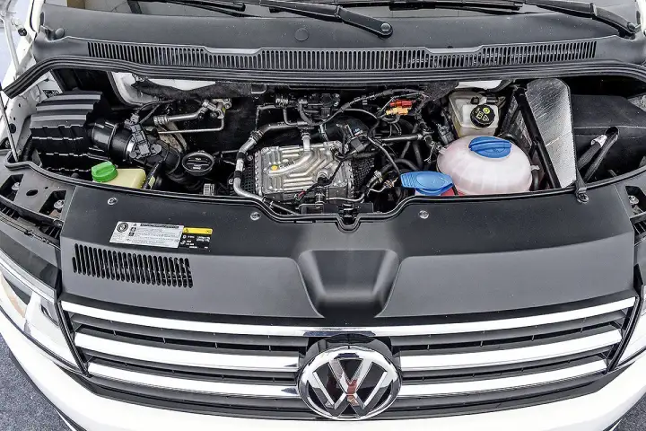 VW T6 150 PS Motorraum mit sichtbaren Leitungen und Kühlmittelbehälter. Mögliche Probleme am Motor sind hier zu sehen.