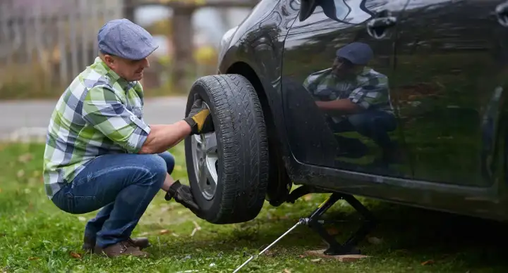 Mann wechselt Reifen mit Reifendrucksensor. Er kniet neben dem Auto, das auf einem Wagenheber steht.